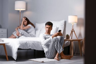 Üzgün genç adam yatak odasında karısıyla tartıştıktan sonra cep telefonu kullanıyor.