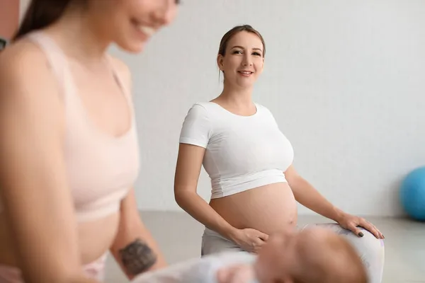 若いです妊娠中の女性ありますヨガとともにトレーナーと小さな赤ちゃんでジム — ストック写真