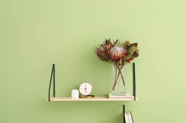 Vazoda egzotik kurumuş çiçekler, yeşil duvarda çalar saat ve kulaklıklar asılı.