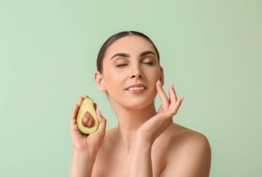 Avokado tutan ve renkli arka planda yüzüne dokunan, gözleri kapalı gülümseyen kadın.