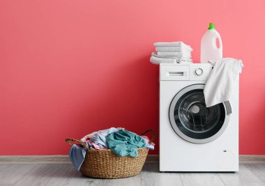 Çamaşır sepeti ve çamaşır makinesi pembe duvarın yanında.
