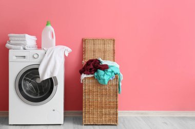Çamaşır sepeti ve çamaşır makinesi pembe duvarın yanında.