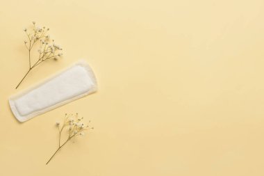 Sarı arka planda regl pedi ve çiçekler