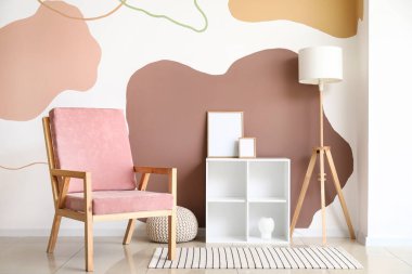 Pembe koltuk, boş çerçeveli raf ünitesi ve renk duvarına yakın lamba.