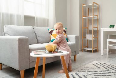 Vücut giysisi içinde tatlı bir kız. Evde kanepenin yanında yürümeyi öğreniyor.