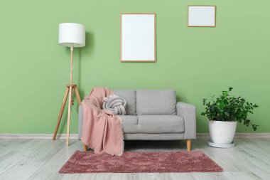 Yeşil duvarda lamba ve boş çerçeve asılı gri kanepe.