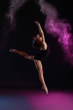 Küçük kız karanlık arka planda jimnastik yapıyor.