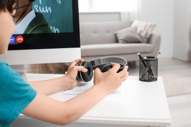 Kulaklıklı küçük çocuk evde internetten çalışıyor.