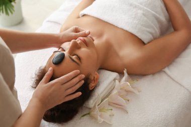 Genç Afro-Amerikalı kadın spa salonundaki terapistle yüz masajı yaptırıyor.
