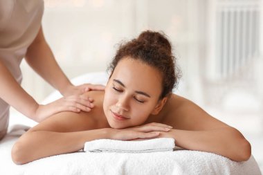Güzeller güzeli Afro-Amerikalı kadın, spa salonunda terapist tarafından masaj yaptırıyor.