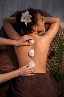 Güzel Afro-Amerikalı kadın masaj yaptırıyor. Spa salonunda terapistin taşlarıyla.