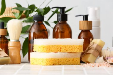 Banyo süngeri, tıraş fırçası, kozmetik ürünleri şişeleri, sabun barı ve fayans masasında deniz tuzu.