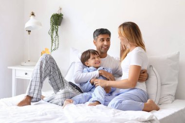Mutlu ebeveynler ve küçük oğulları yatakta oturuyor.