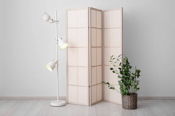 Stylish folding screen with lamp and houseplant in room interior