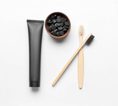 Aktif karbon diş macunlu tüp, beyaz arka planda haplı kase ve diş fırçası.