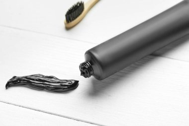 Beyaz ahşap arka planda aktif karbon diş macunu bulunan tüp, yakın plan.