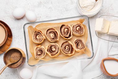 Pişmemiş tarçınlı çörekler ve beyaz arka plandaki malzemeler.