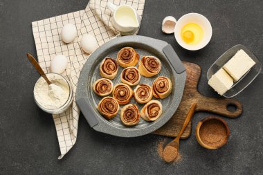 Pişmemiş tarçınlı çörekler ve siyah arka plandaki malzemeler.