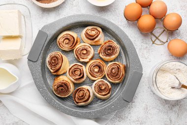 Pişmemiş tarçınlı çörekler ve beyaz arka plandaki malzemeler.