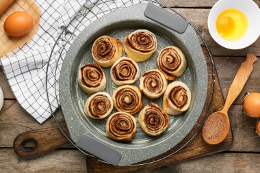 Pişmemiş tarçınlı çörekler ve ahşap zemin üzerindeki malzemeler.