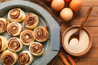 Pişmemiş tarçınlı çörekler ve ahşap arka planda malzemeler, yakın plan.