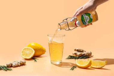 Kadın şişeden limon ve zencefilli taze kombu çayı renkli arka planda cama döküyor.