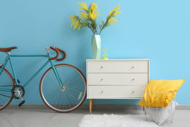 Mavi duvarın yanında vazo, yastık ve bisikletli çekmeceler.