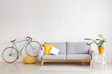 Gri kanepe, ev bitkisi olan merdiven ve beyaz tuğla duvarın yanında bisiklet.