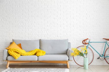 Beyaz tuğla duvarın yanında gri kanepe, bisiklet ve vazo