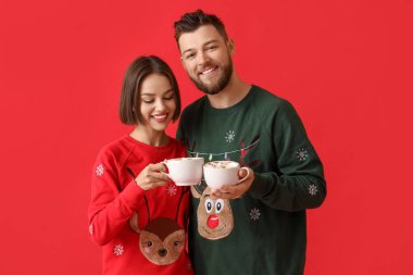 Şık Noel elbiseli genç bir çift ve renkli arka planda sıcak çikolata bardakları var.