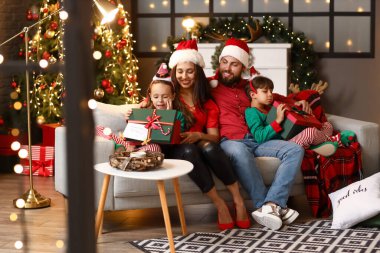 Mutlu çocuklu bir aile ve hediyeler Noel arifesinde evdeki kanepede oturuyor.