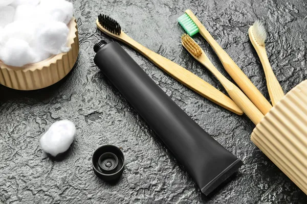 Opened tube with activated carbon toothpaste,  holder with bamboo toothbrushes and cotton balls on dark background, closeup