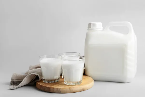 Gallon bottle and glasses of milk on light background