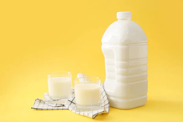 Gallon bottle and glasses of milk on yellow background