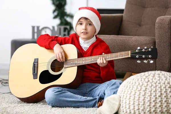 Pikkupoika Joulupukin Hatussa Soittaa Kitaraa Kotona — kuvapankkivalokuva