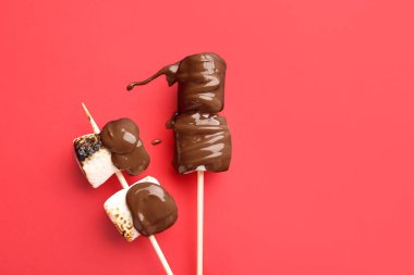 Kırmızı arka planda çikolatalı, lezzetli ızgara şekerlemeli şişler.