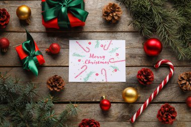 İçinde Merry Noeli, köknar ağacı dalları, Noel baloları ve tahta arka planda hediye kutuları olan tebrik kartı.