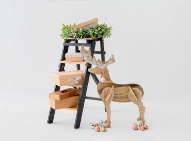 Tahta ren geyiği, hediye kutularıyla merdiven ve beyaz arka planda Noel çelengi.