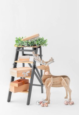 Tahta ren geyiği, hediye kutularıyla merdiven ve beyaz arka planda Noel çelengi.