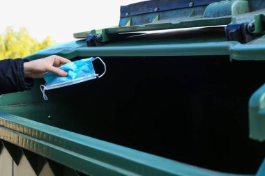 Dışarıdaki plastik konteynıra kullanılmış maske atan kadın.