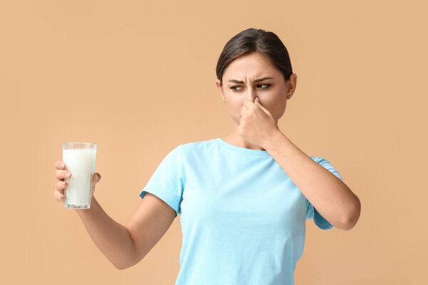 Young woman refusing to drink milk on color background
