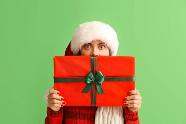 Beautiful young woman in Santa hat with big Christmas gift on green background