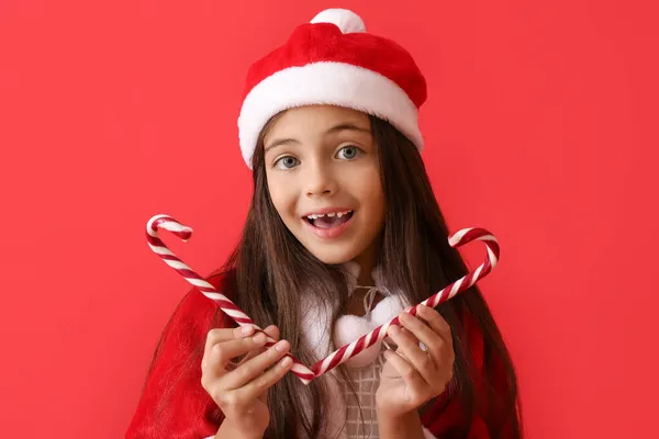 Nettes Kleines Mädchen Mit Weihnachtsmütze Und Zuckerstangen Auf Farbigem Hintergrund — Stockfoto