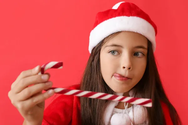 可爱的小女孩戴着圣诞礼帽 背景是彩色的糖果手杖 — 图库照片