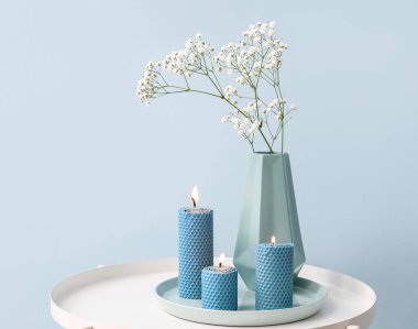 Güzel yanan mumlar ve vazolar. Renkli duvarın yanındaki masada çiçekler.