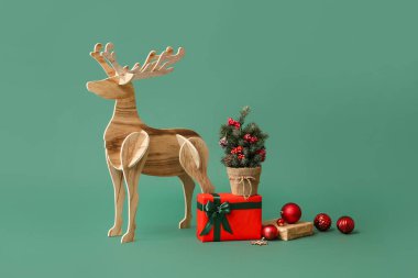 Küçük Noel ağacıyla ahşap ren geyiği ve yeşil arka planda hediyeler.