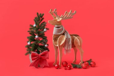 Kırmızı arka planda eşarplı tahta ren geyiği ve Noel ağacı
