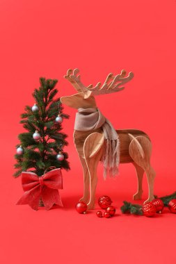 Kırmızı arka planda eşarplı tahta ren geyiği ve Noel ağacı