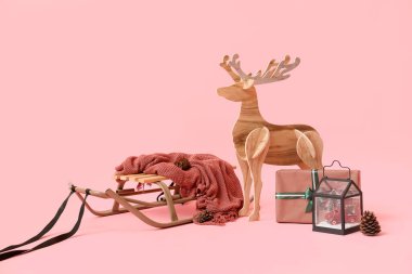Ahşap rengeyiği, kızak ve pembe arka planda Noel hediyesi.