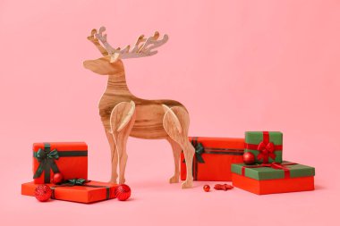 Pembe arka planda Noel hediyeleri olan tahta ren geyiği
